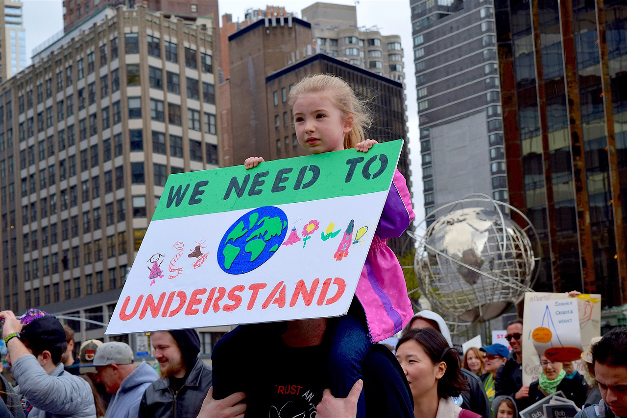 Young girl on adult's shoulders holding sign at march for science event